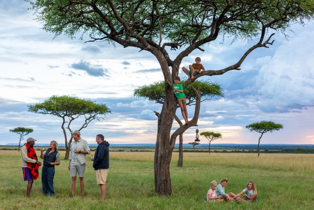 Children playing on a tree whilst the parents enjoy a sundowner on the Masai Mara plains