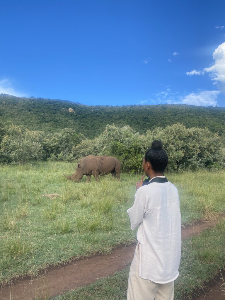 A tourist on a walking safari looking at a rhino, wearing neutral colours