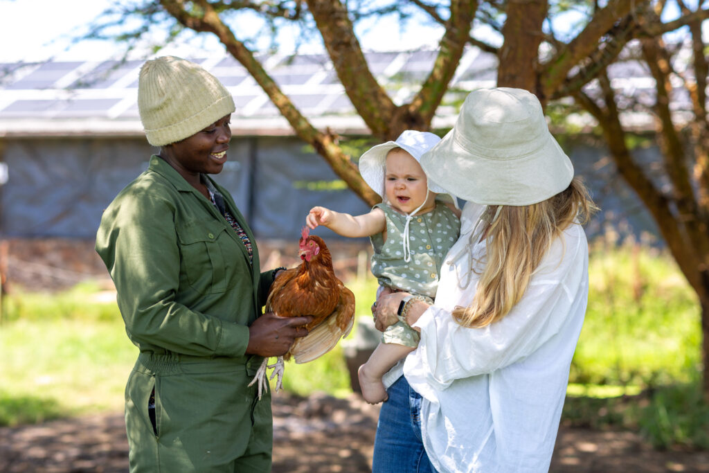 A mum and child with sun hats on speaking to a staff member with a chicken on safari
